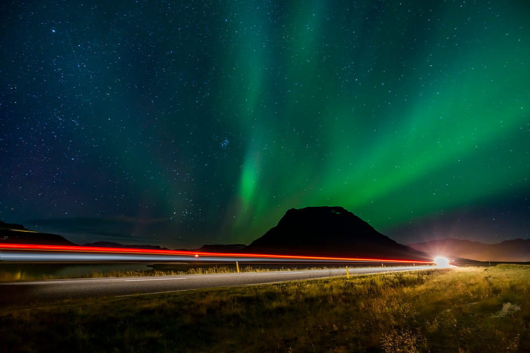 Northern Lights near the highway with a mountain in the backdrop