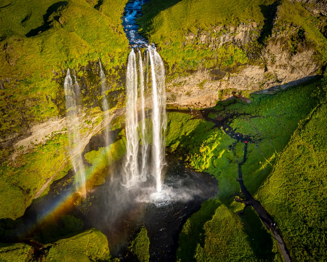 aerial view of Seljalandfoss with a faint rainbow and bright green moss 