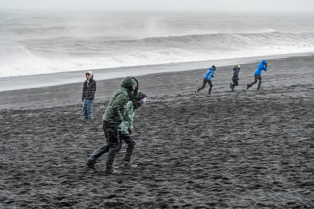 tourists in bad weather at reynisfjara iceland with waves in background