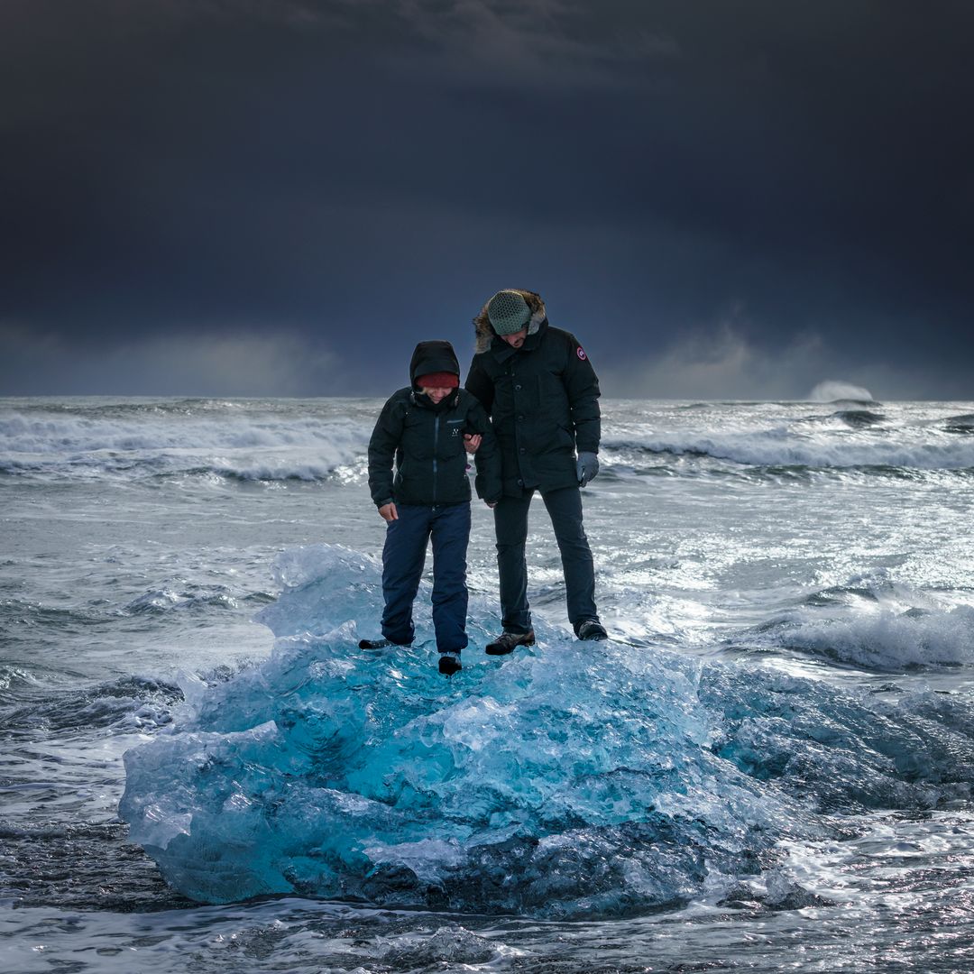 tourists standing on a small iceberg in on diamond beach