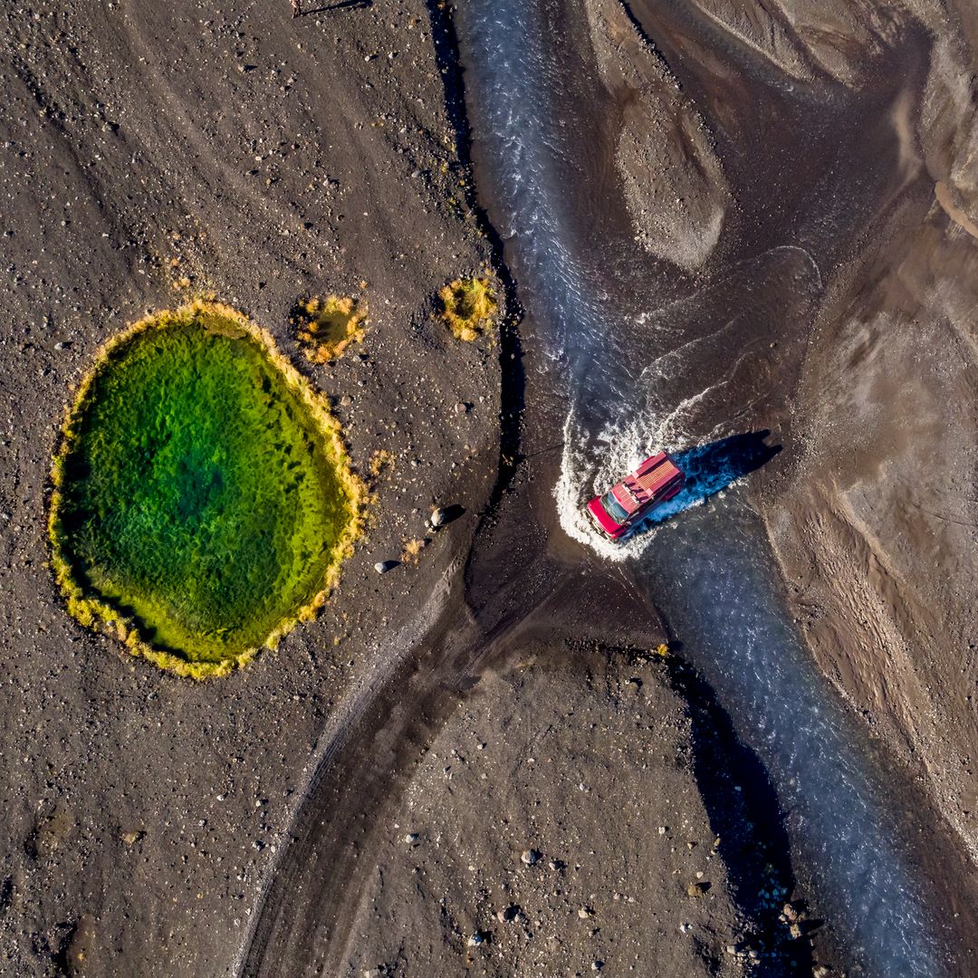 a jeep driving through water with black sand all around in Thorsmork
