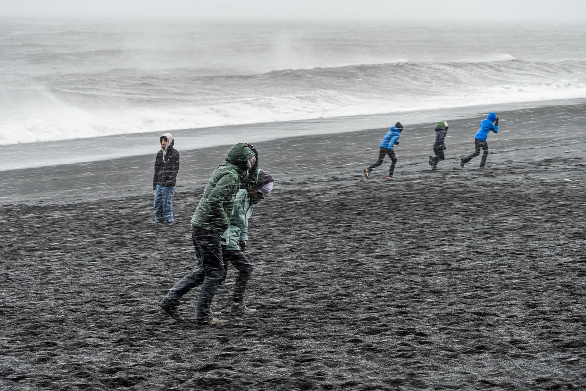 tourists in bad weather at reynisfjara iceland with waves in background