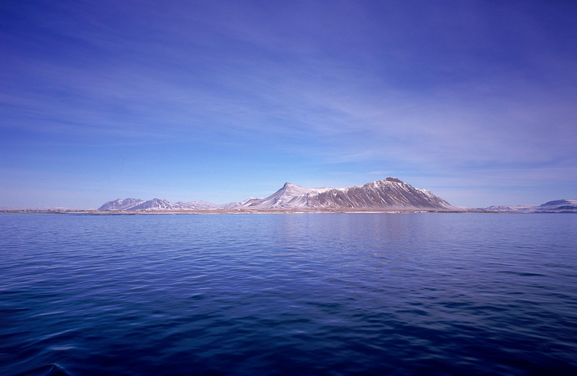 a snowdusted mountain off the coast of the ocean with a blue sky background